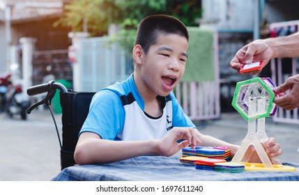 Disabled Child On Wheelchair Is Interested In Skills Development Toy On Home Nature Background,Special Children's Lifestyle,Life In The Education Age Of Special Need Kids,Happy Disability Kid Concept.