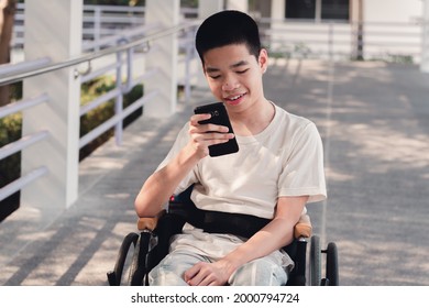 Disabled Child On Wheelchair Using Technology With Nature Background Around Hospital, Lifestyle In The Education Age Of Special Need Kid, Happy Disability Teen Use Smartphone And Social Media Concept.