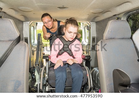 A disabled child in a wheelchair being helped into a specially adapted van / Working with disability