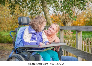 A Disabled Child In A Wheelchair Relaxing Outside Together With A Voluntary Care Worker.