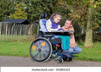 Disabled Child In Wheelchair Relaxing Outside Together  With A Care Assistant / Working With Disability