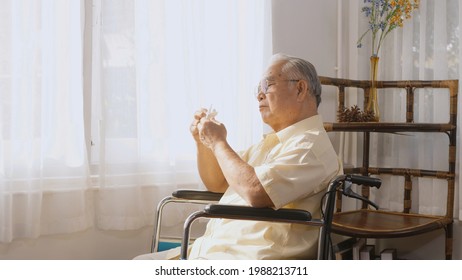 Disabled Elderly Patient Sit On Wheelchair Alone Look Through Window Playing Origami Paper Bird, Sad Asian Senior Old Man Feel Lonely Waiting Take Care White Room Dementia And Alzheimer