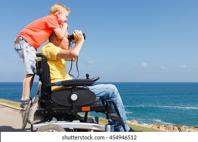 Disabled father looking through binoculars while his young boy 