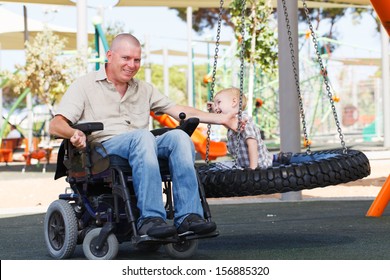 Disabled Father Play With His Little Son On The Playground