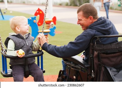 Disabled Father Play With His Little Son On The Playground.