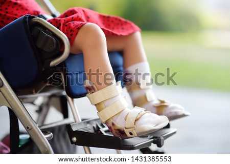 Disabled girl sitting in wheelchair. On her legs orthosis. Child cerebral palsy. Inclusion. Family with disabled kid.