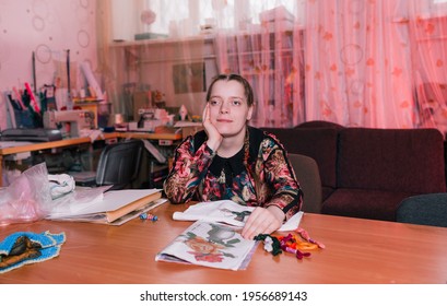 A Disabled Girl With Slanted Eyes Sits At A Table And Smiles. People With Disabilities.