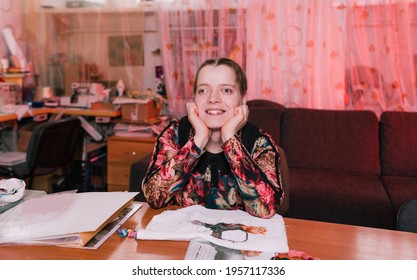 A Disabled Girl With Slanted Eyes Sits At A Table And Smiles.