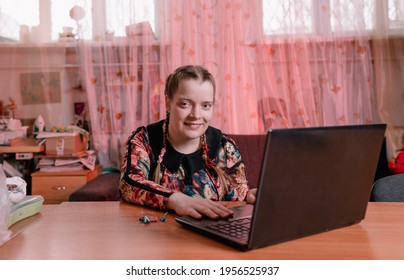 a disabled girl with slanted eyes is sitting at a desk and working on a laptop.
