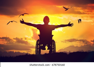 Disabled handicapped man has a hope. He is sitting on wheelchair and stretching hands at sunset.