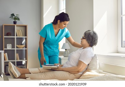 Disabled lady elderly patient and friendly female nurse talking at hospital ward. Old woman lying on bed and rest with book. Caregiver offering help. Nursing home for retired person and medical care - Powered by Shutterstock