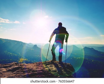 Disabled man with forearm crutches on the edge. View over the hilly ladscape in summer evening. Hurt leg on bandage with crutches