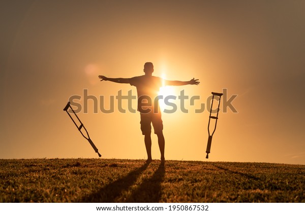 A disabled man letting go of his crutches\
facing the sunset. Healing medical concept of cure, recovery,\
miracle, hope, insurance