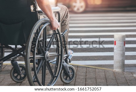 Disabled man on wheelchair preparing to cross the road on pedestrian crossing, copy space.