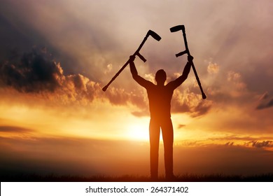 A disabled man raising his crutches at sunset. Positive concept of cure, recovery, medical miracle, hope, insurance etc. 