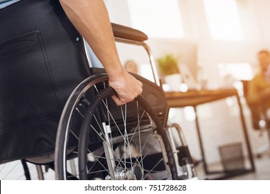Um homem deficiente está sentado em uma cadeira de rodas. Ele segura as mãos no volante. Perto estão seus colegas.