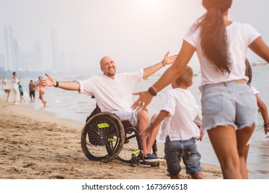 Disabled Man In A Wheelchair With His Family On The Beach.