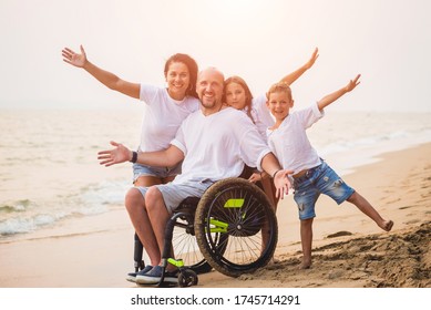 Disabled Man In A Wheelchair With His Family On The Beach.