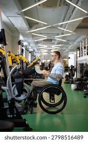 Disabled man in wheelchair using upper body ergometer for recovery after spinal injury, hand cycling machine helps build muscles strength. Male with spinal injury undergoing long-term rehabilitation.