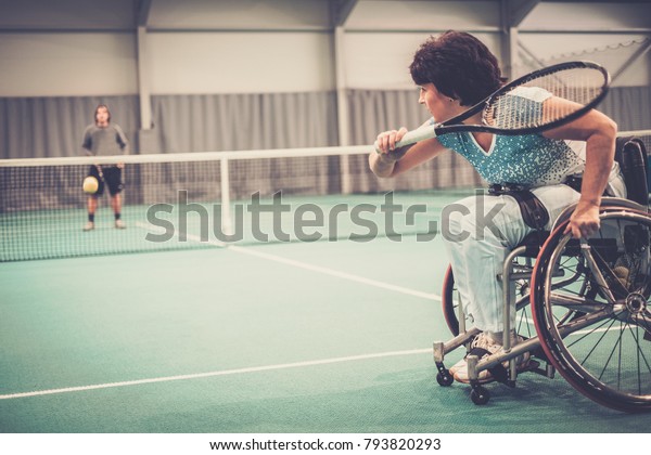 Disabled mature woman on wheelchair playing tennis\
on tennis court.