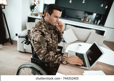 Disabled In Military Uniform, He Works For His Laptop. He Sits At His Desk. He Is In His Large Modern Apartment.