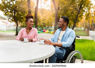 Disabled millennial black guy in wheelchair having date with lovely woman in outdoor cafe, drinking coffee, enjoying friendly talk at autumn park. Impaired couple having romantic times outside - Powered by Shutterstock