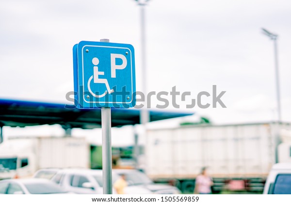 Disabled parking sing in transport station,\
wheelchair people street place on blurred cars and refill fuel pump\
station, white and blue\
sing