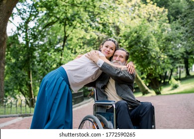 Disabled People, Palliative Care. Lifestyle Summer Portrait Of Senior Bearded Man In Wheelchair Hugging His Young Pretty Hipster Granddaughter, Walking In Park Outdoors