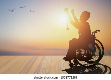 Disabled Person Silhouette Winners Hand Holding Gold Medal Top Of Wheelchair Have Sunset Background. International Disability Day And Handicapped Paralympics. Challenge, Conquer And Healthcare Concept