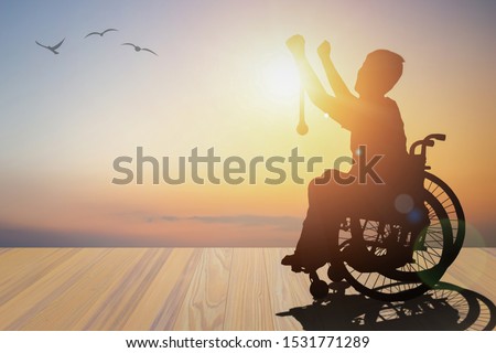 Disabled person silhouette winners hand holding gold medal top of wheelchair have sunset background. International Disability Day and Handicapped Paralympics. Challenge, Conquer and healthcare concept