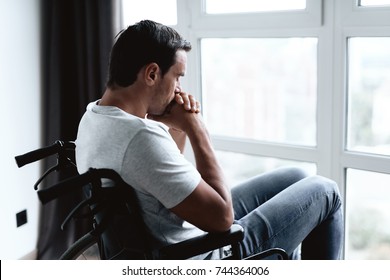 A Disabled Person In A Wheelchair Sits In Front Of A Large Panoramic Window And Is Sad. He Looks Out The Window. He Is In His Modern Apartment.