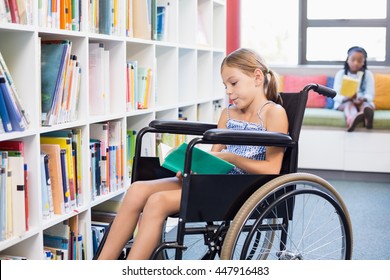 Disabled school girl reading book in library at school