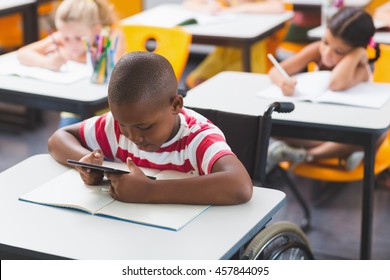Disabled schoolboy using digital tablet in classroom at school
