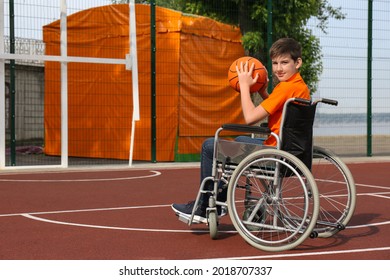 Disabled Teenage Boy In Wheelchair With Basketball Ball At Outdoor Court