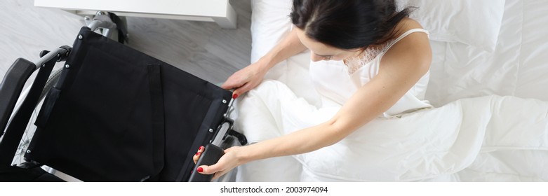 Disabled woman gets out of bed and holds onto wheelchair - Powered by Shutterstock