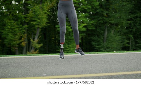 Disabled Woman Jumping Sideways On Road. Fit Girl Jumping On Asphalt Road In Slow Motion. Active Runner Training Outdoors Alone