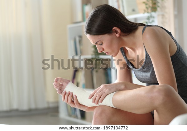 Disabled woman wearing\
bandaged feet complaining suffering ankle ache sitting on a couch\
at home
