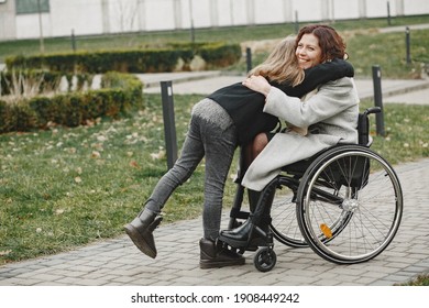 Disabled woman in wheelchair with daughter. Family walking outside at park.