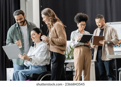 disabled woman in wheelchair discussing startup project on laptop with happy interracial colleagues - Powered by Shutterstock