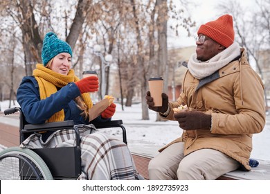 Disabled Woman In Wheelchair Drinking Hot Tea With African Man In Winter Day Outdoors