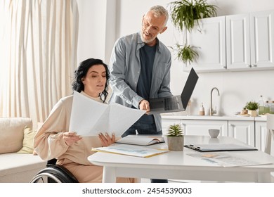 A disabled woman in a wheelchair and her husband collaborate on paperwork in their kitchen at home. - Powered by Shutterstock