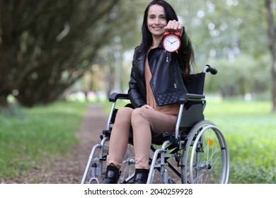 Disabled Woman In Wheelchair Holding Red Alarm Clock In Park