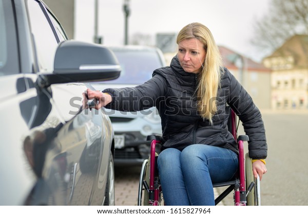 Disabled woman in a wheelchair opening a car\
door from the street in a concept of adapting and mobility of the\
handicapped