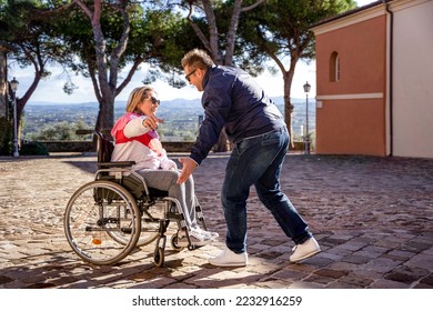 Disabled women on wheelchair with man outside - Son and mother are about to hug - Happy family having fun together outdoors - Warm filter - Shutterstock ID 2232916259