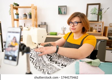 Disabled Young Dressmaker In Eyeglasses Using Sewing Machine While Giving Online Class On Sewing