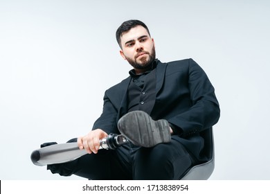 Disabled Young Man With Prosthetic Leg Sitting On A Chair In Studio Over White Background, Artificial Limb Concept