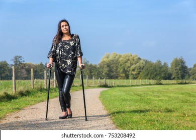 Disabled Young Woman Walking On Crutches In Park