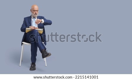 Disappointed businessman sitting on a chair and waiting, he is checking the time