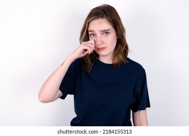 Disappointed dejected young caucasian woman wearing black T-shirt over white background wipes tears stands stressed with gloomy expression. Negative emotion