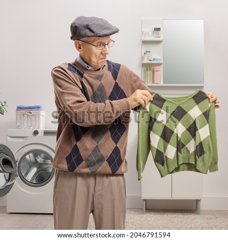 Disappointed elderly man holding a shrunken blouse in a bathroom